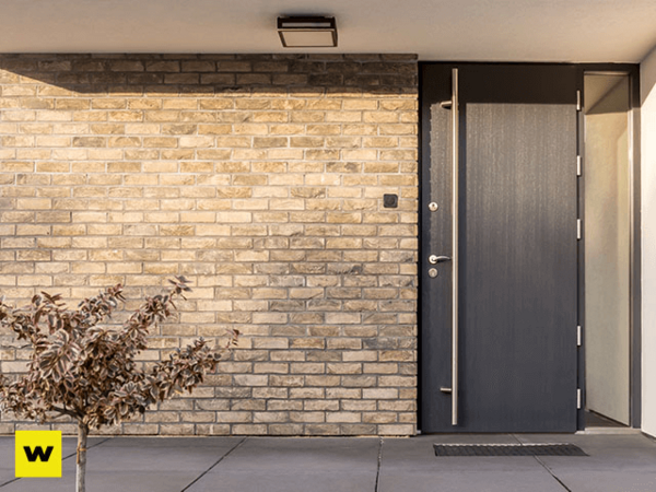 Moderne Haustür aus Aluminium neben heller Klinkerfassade mit kleiner Pflanze im Eingangsbereich.